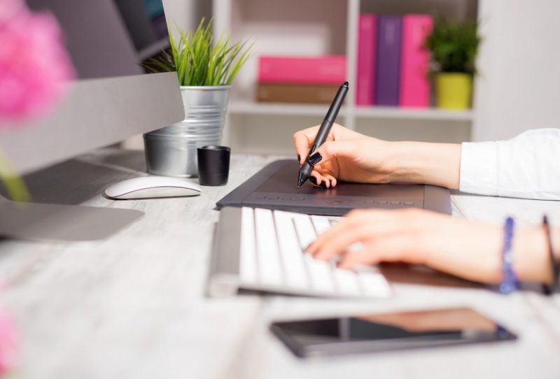 person writing something with pen and other hand on the keyboard